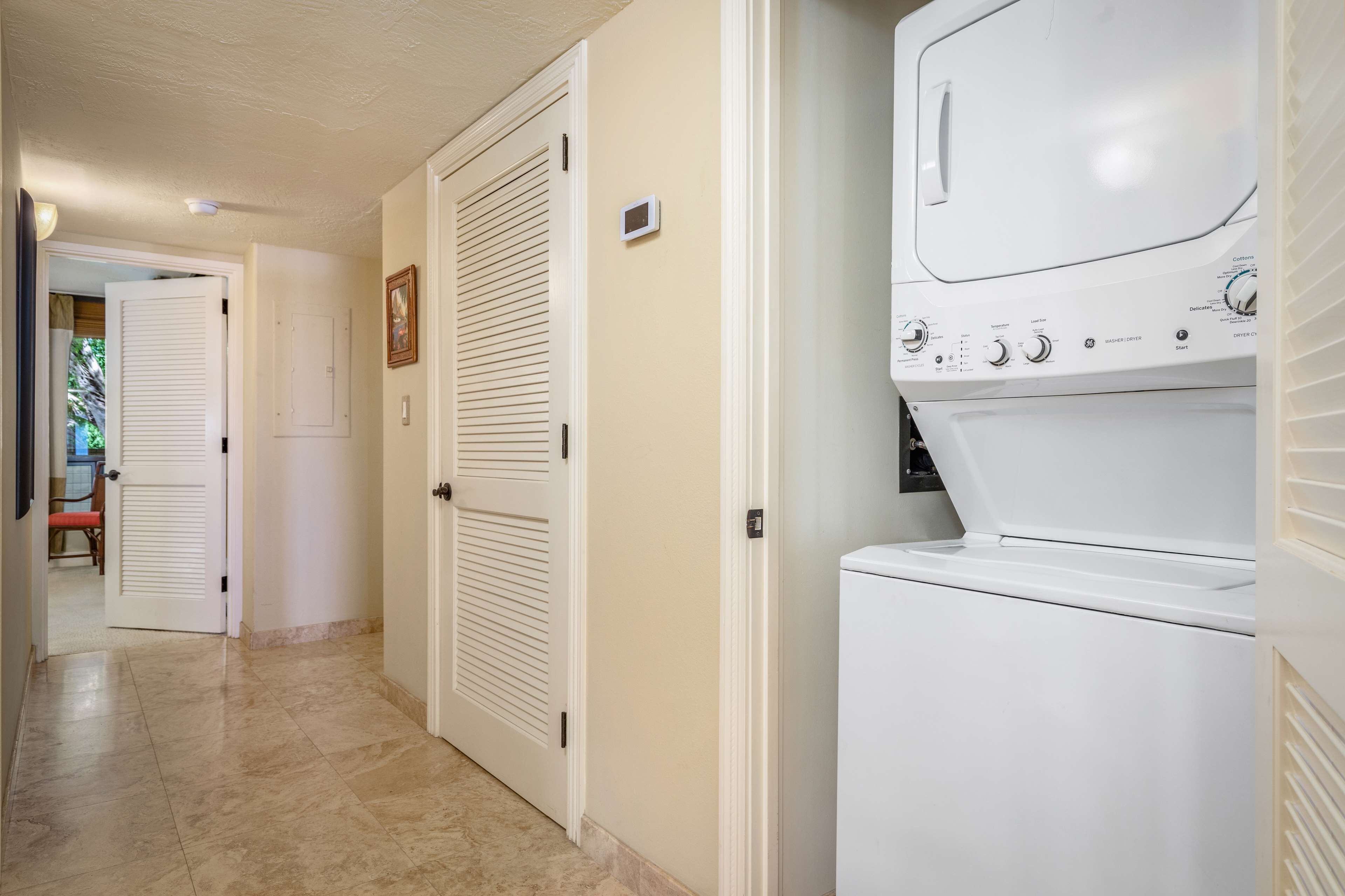 A laundry room with a front-loading washer and dryer, beige tiled floor, and white doors.