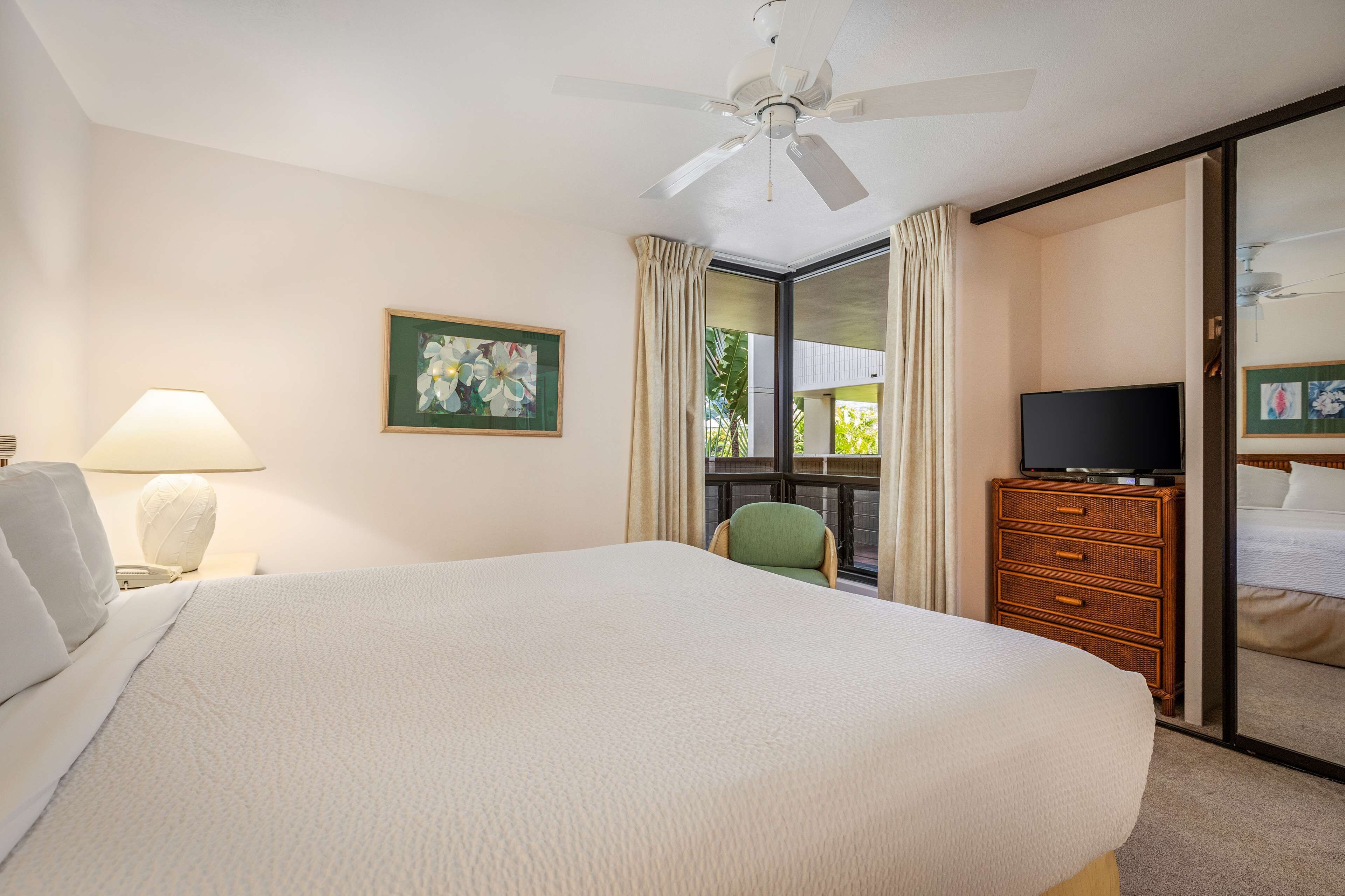Habitación de hotel con una cama grande, televisor, cómoda, silla, ventana con cortinas y ventilador de techo.