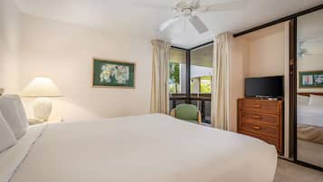 Habitación de hotel con una cama grande, televisor, cómoda, silla, ventana con cortinas y ventilador de techo.