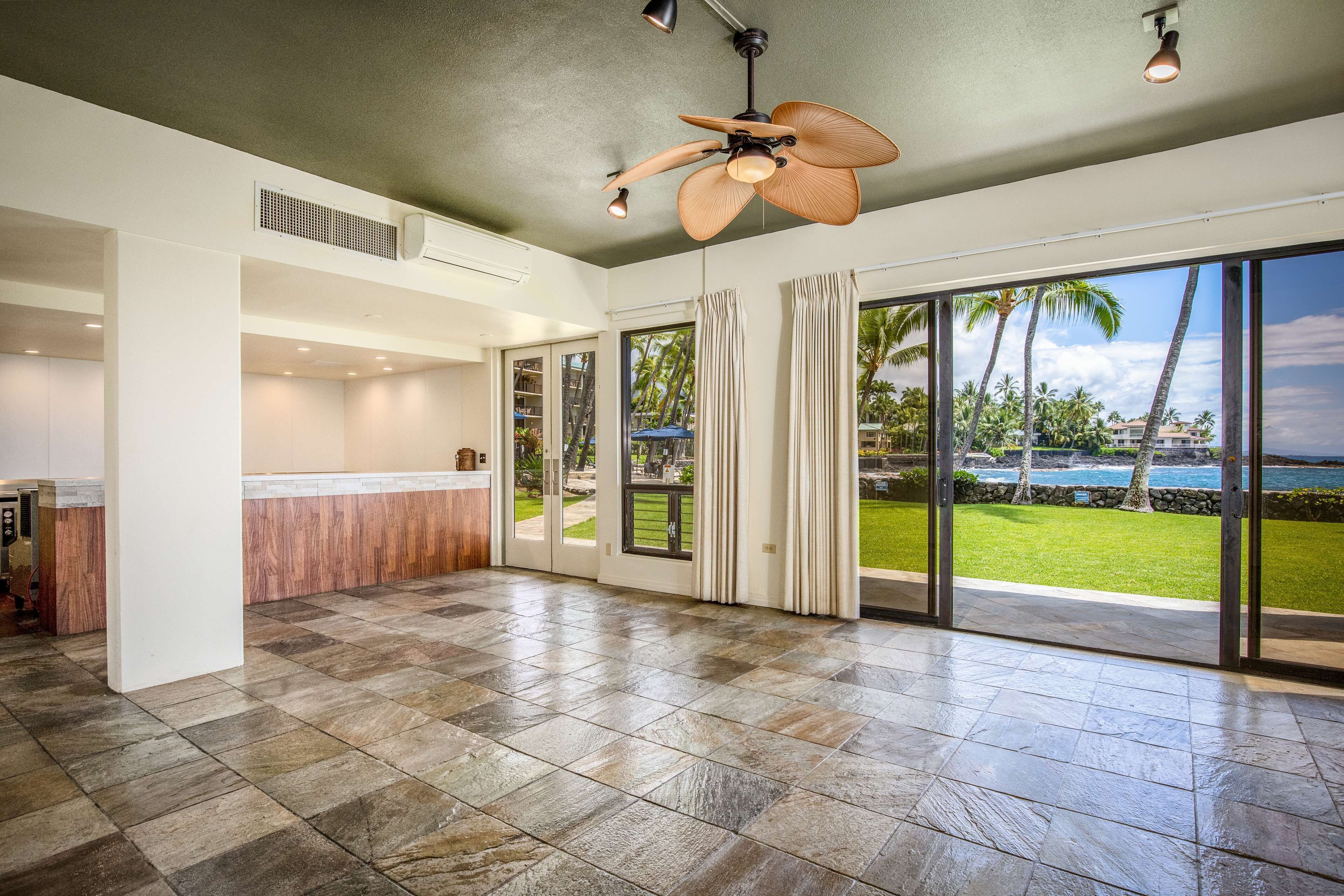 A spacious room with a large sliding glass door leading to a balcony with a view of palm trees and the ocean.