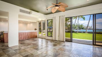 A spacious room with a large sliding glass door leading to a balcony with a view of palm trees and the ocean.