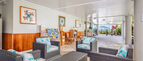 A covered outdoor seating area with wicker furniture and framed artwork on the walls.