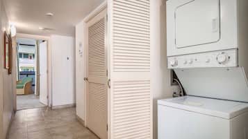 Un cuarto de lavandería con lavadora y secadora, una puerta con ventanal y vista a un balcón al fondo.
