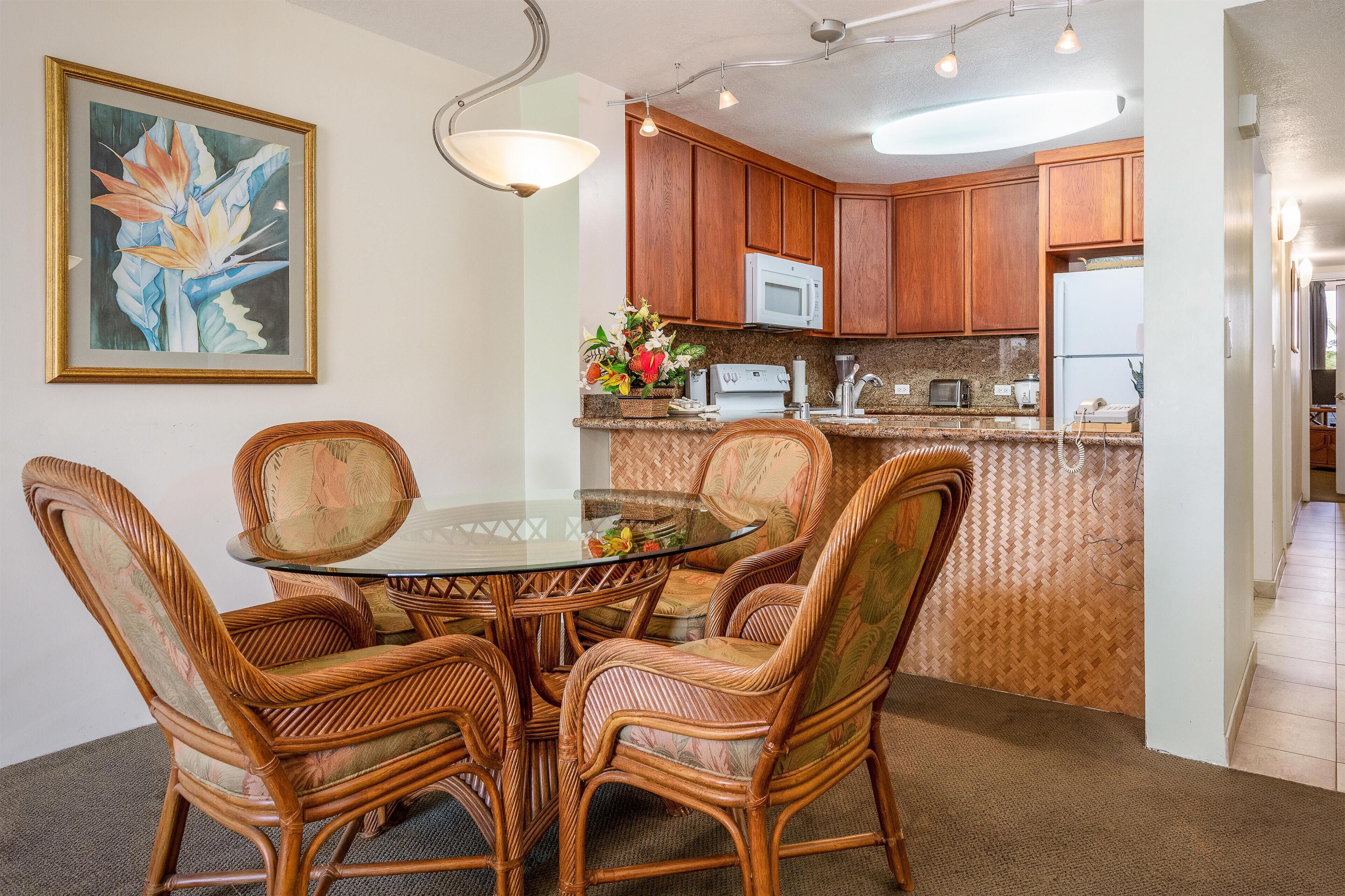 A dining area with a glass table surrounded by wicker chairs, a kitchen with wooden cabinets, and a microwave above the counter.