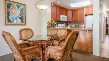 A dining area with a glass table surrounded by wicker chairs, a kitchen with wooden cabinets, and a microwave above the counter.