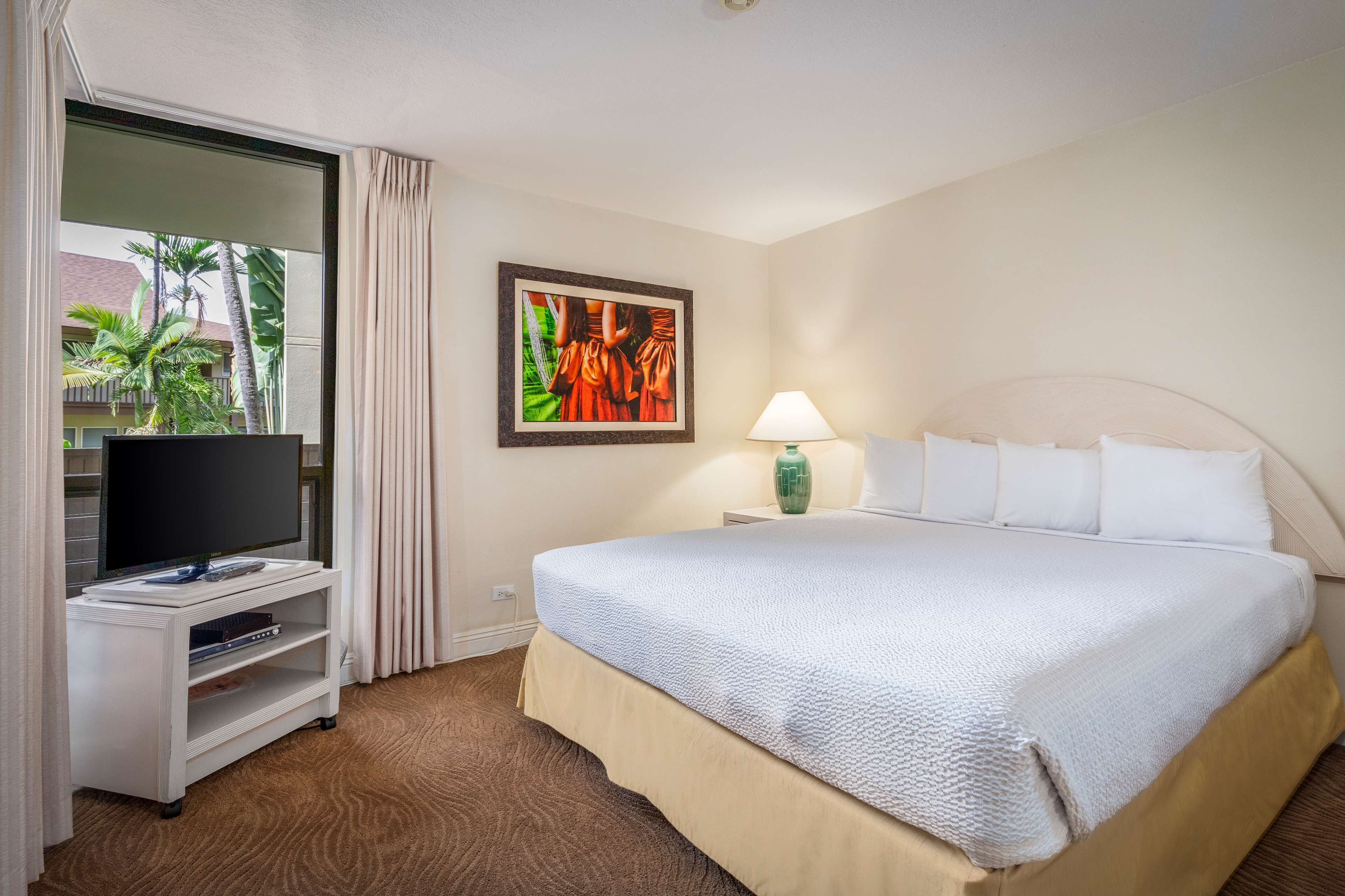 A hotel room with a bed, a TV on a stand, a painting on the wall, and a window with curtains.