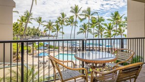 Un balcon avec vue sur une plage et des palmiers, une piscine et un espace salon extérieur.