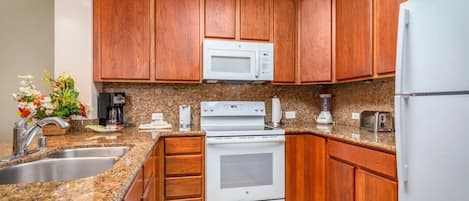A kitchen with wooden cabinets, a white microwave, a stove, a sink, and a refrigerator.