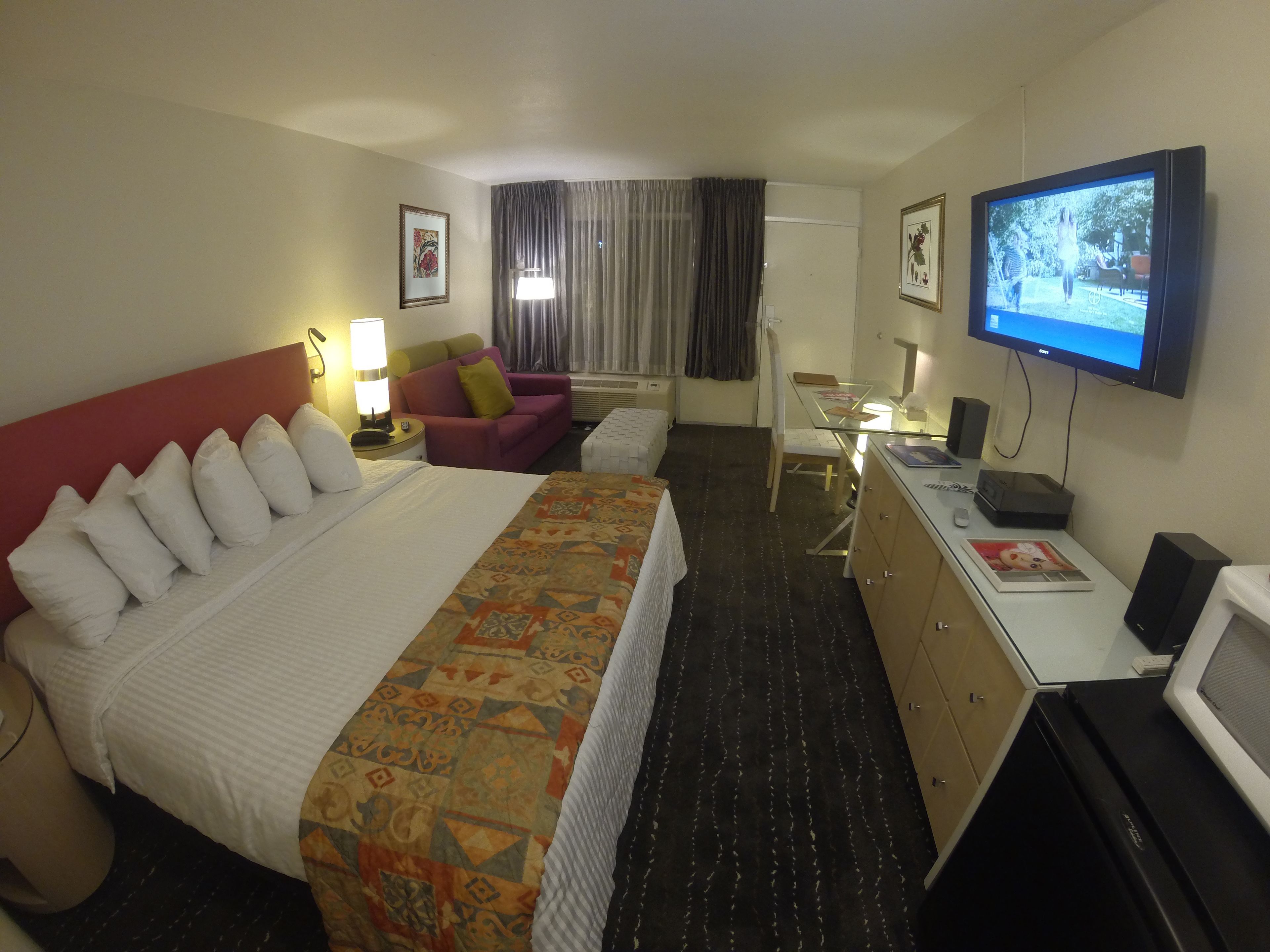 A hotel room with a large bed, a desk with a computer, a television, and a window with curtains.