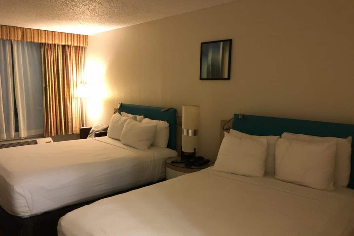 A hotel room with two beds, a nightstand with a lamp, a telephone, and a painting on the wall.