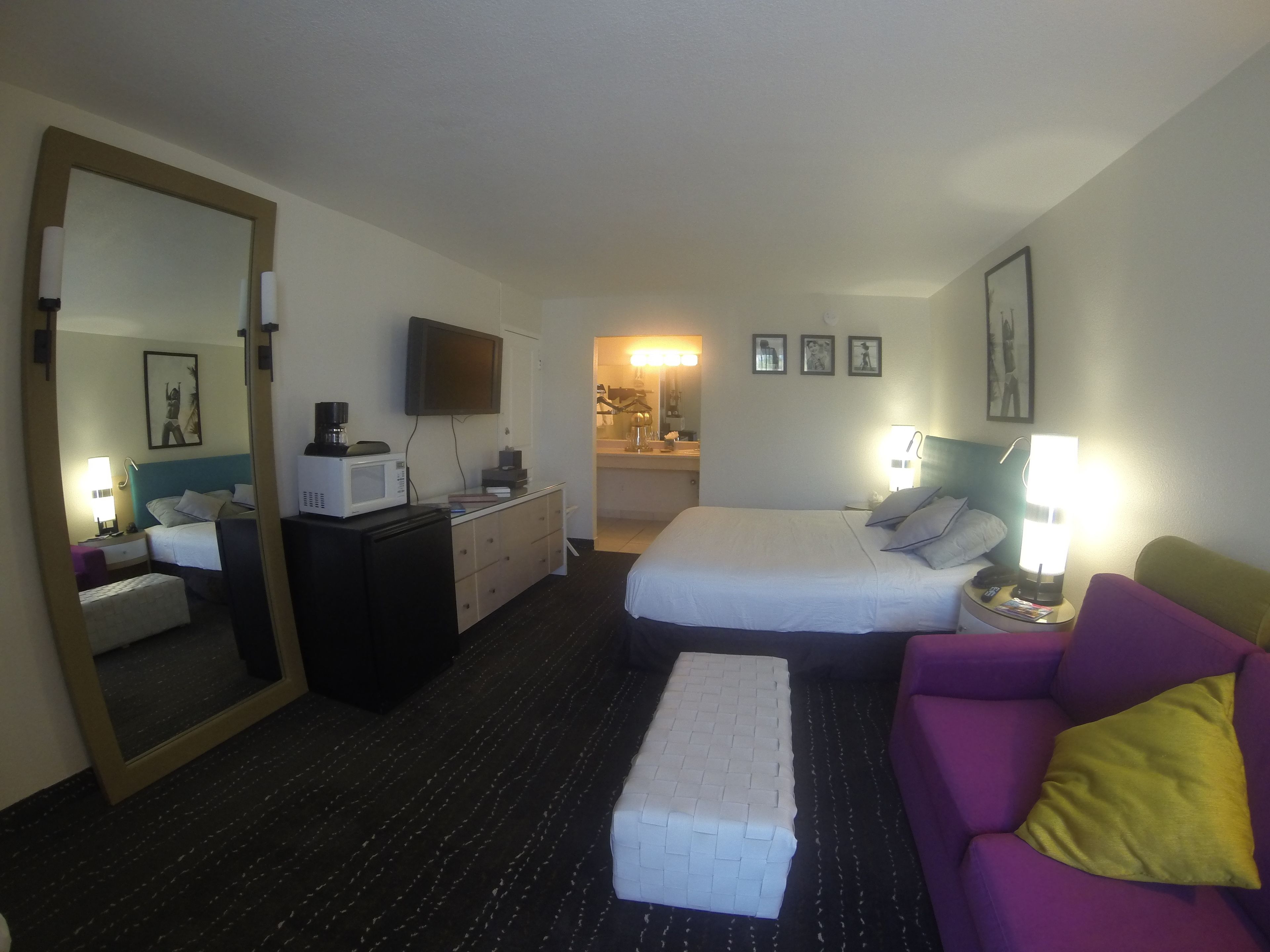 Hotelkamer met een bed, een slaapbank, een bureau, een dressoir, een spiegel, een televisie en een badkamer zichtbaar door een open deur.