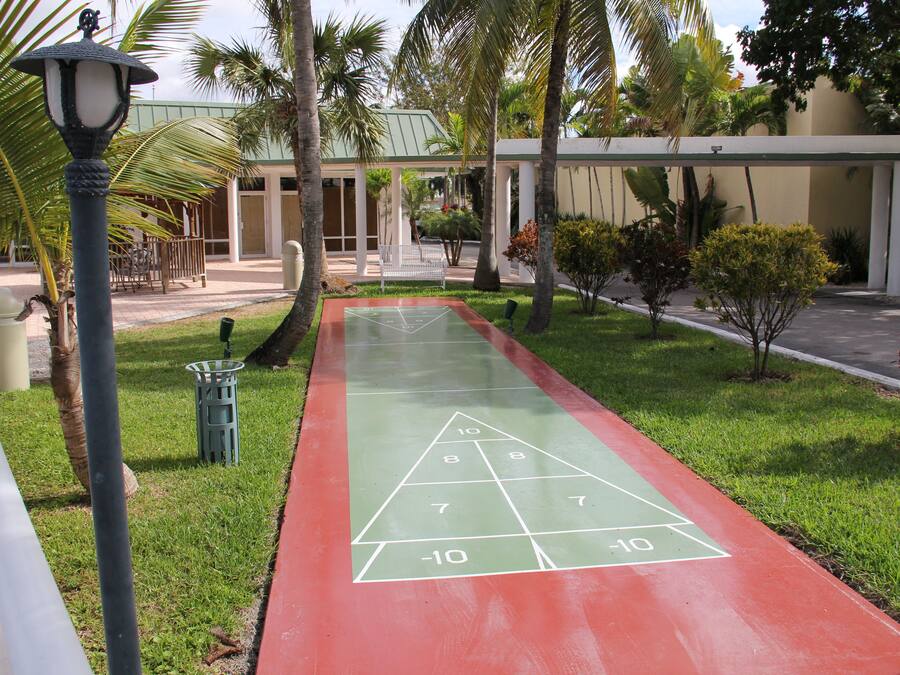 Ein Shuffleboardfeld mit grüner und roter Oberfläche, umgeben von Palmen und einem Gebäude mit grüner Dachbegrünung.