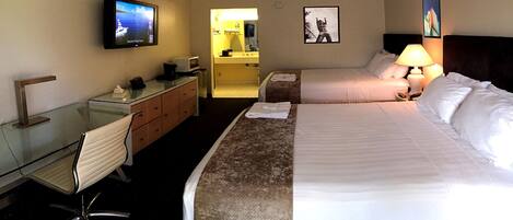 A hotel room with a bed, a desk, a chair, a TV, a bathroom, and a nightstand with a lamp.