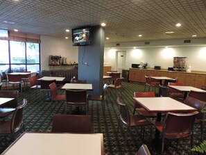 A restaurant with tables and chairs, a kitchen area, and a television mounted on the wall. - Floridian Hotel (Homestead)