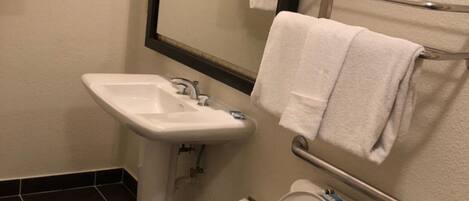 A bathroom with a sink, mirror, toilet, and handrails.