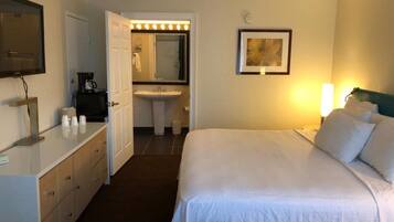 Una camera d'albergo con un letto, una scrivania con uno specchio, un lavandino e un quadro appeso al muro.