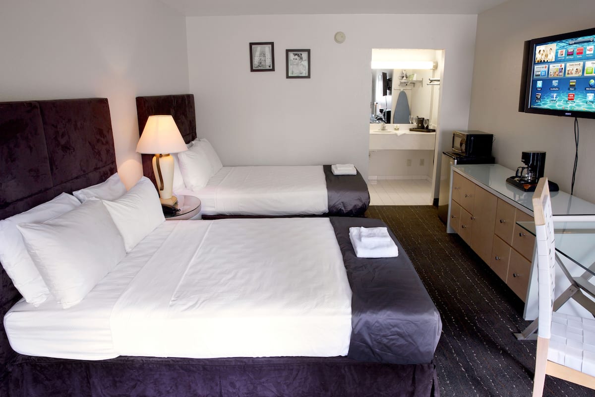 A hotel room with two beds, a TV, a desk, and a bathroom visible through an open door.
