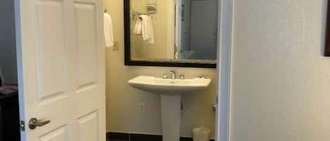 Un bagno d'albergo con un lavandino bianco, uno specchio e una porta che dà su un'altra stanza.