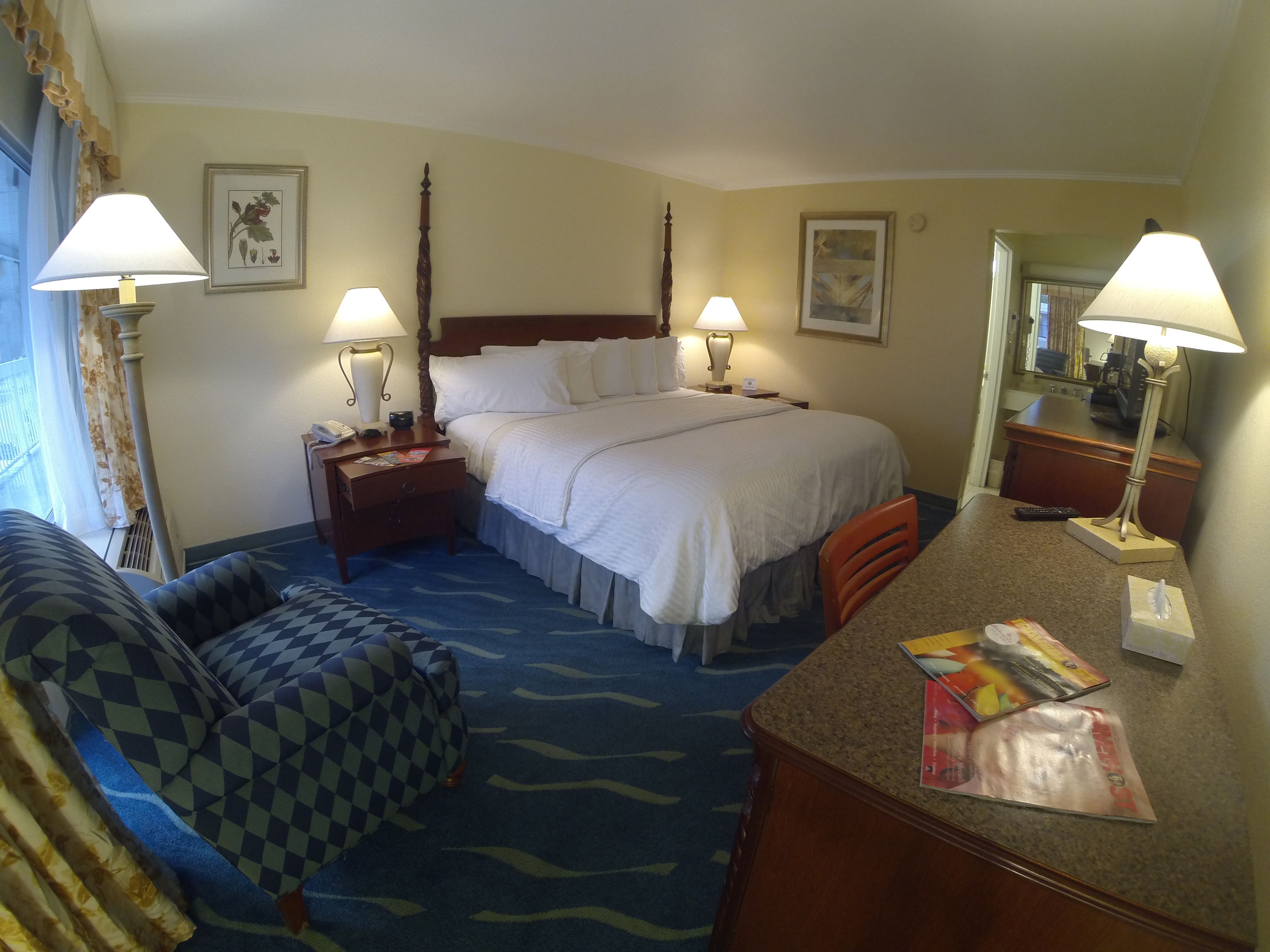 A hotel room with a bed, two bedside tables with lamps, a chair, a desk with a lamp, and a mirror.