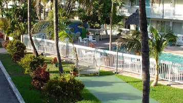 Un área de piscina con valla blanca, sillas de descanso y palmeras.