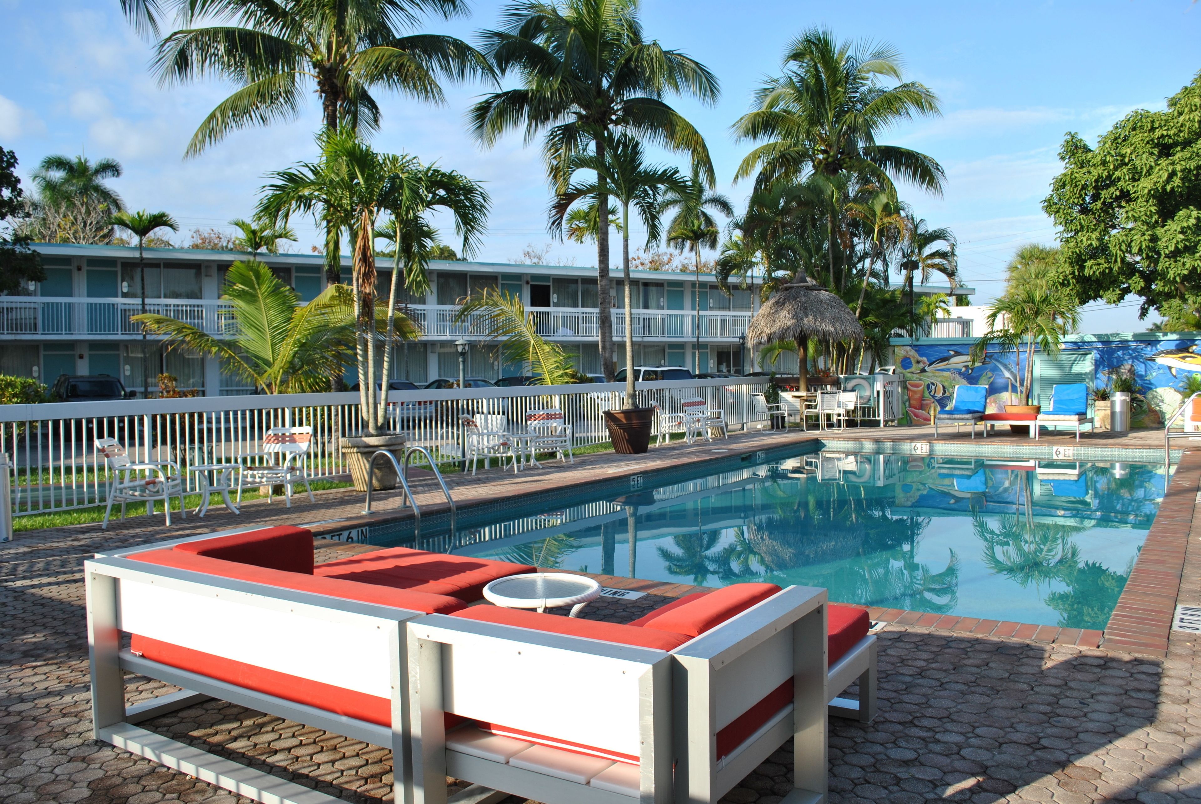 A pool area with lounge chairs and a small table, surrounded by palm trees and a building with balconies.