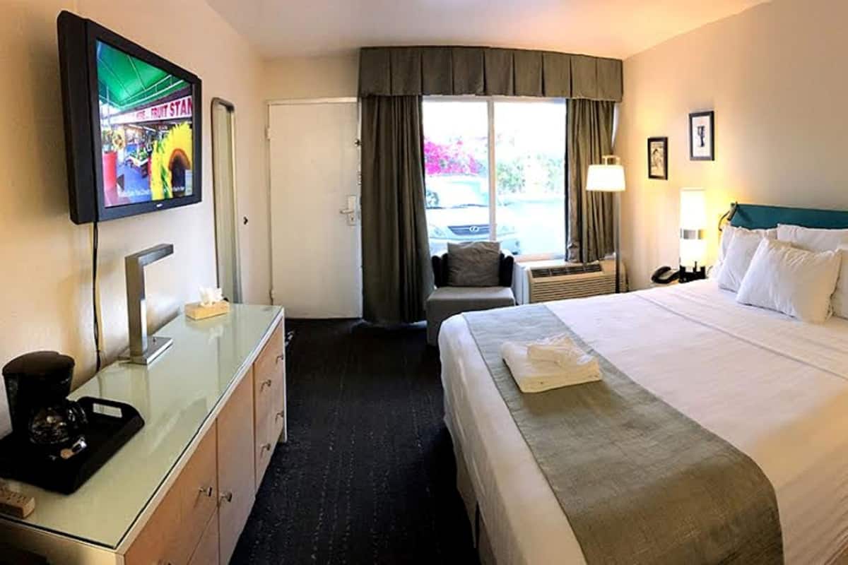 A hotel room with a bed, a desk with a TV, a chair, a window with curtains, and a view of the outside.