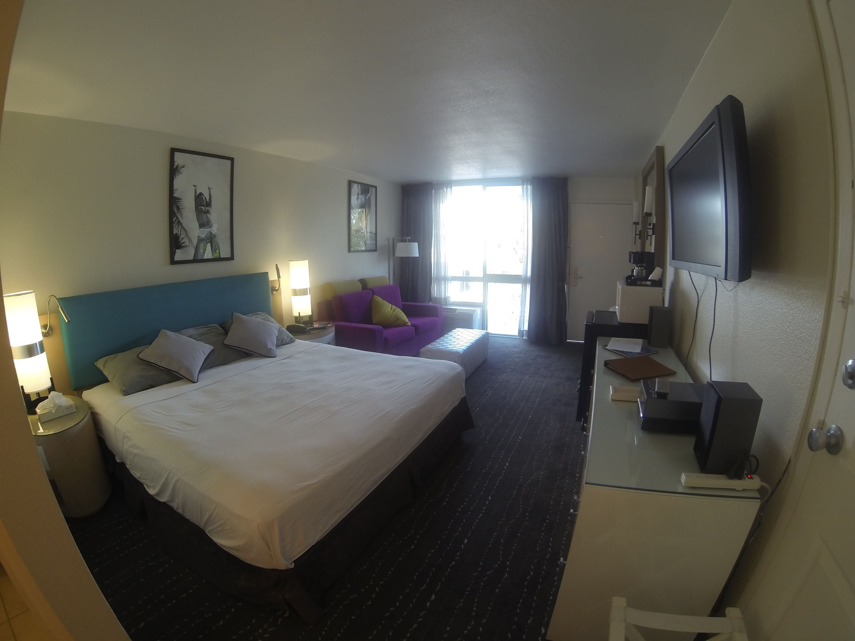 Habitación de hotel con dos camas, un escritorio con computadora, televisión y ventana con cortinas.
