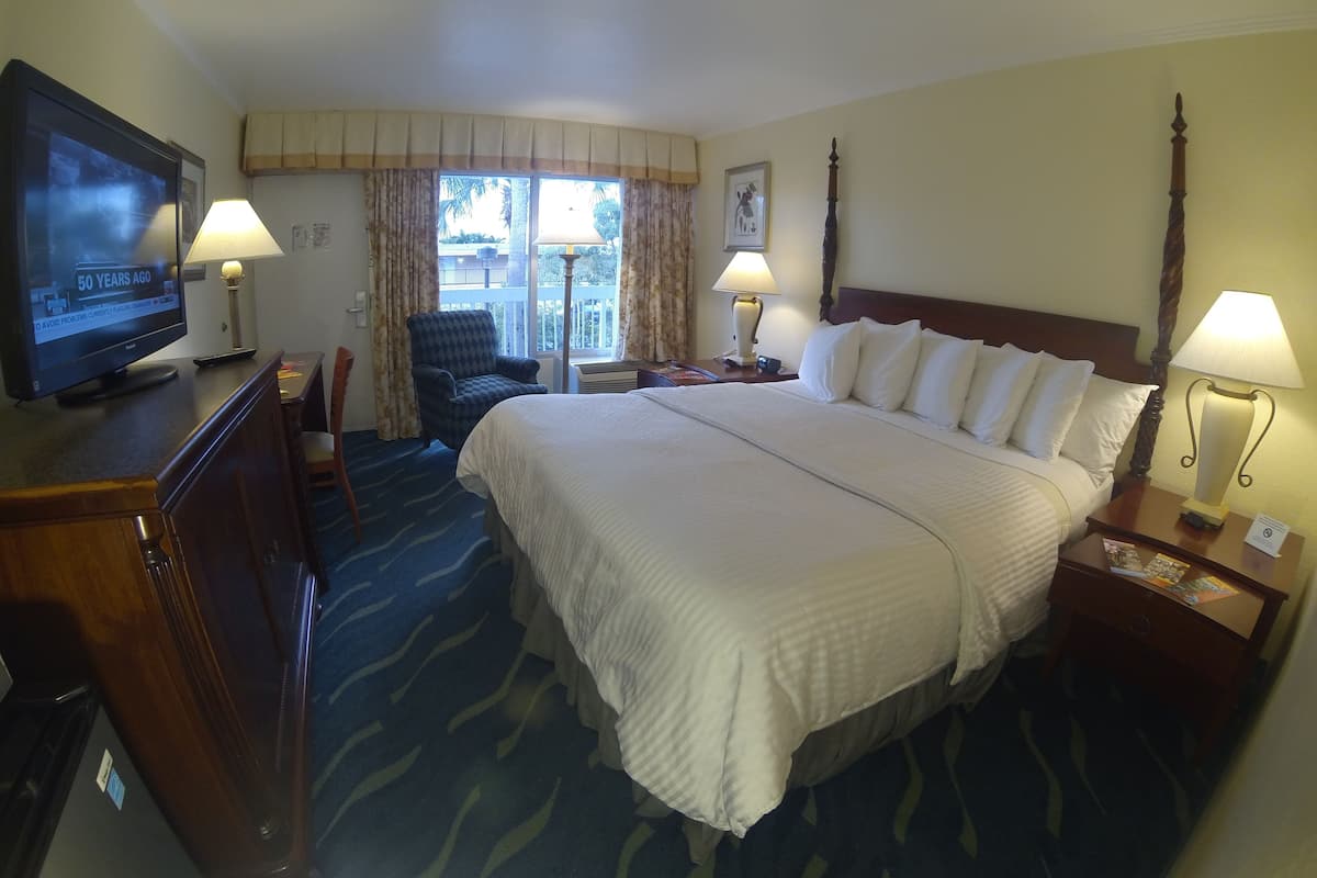 A hotel room with a large bed, two bedside tables with lamps, a television on a dresser, a chair, and a window with curtains.