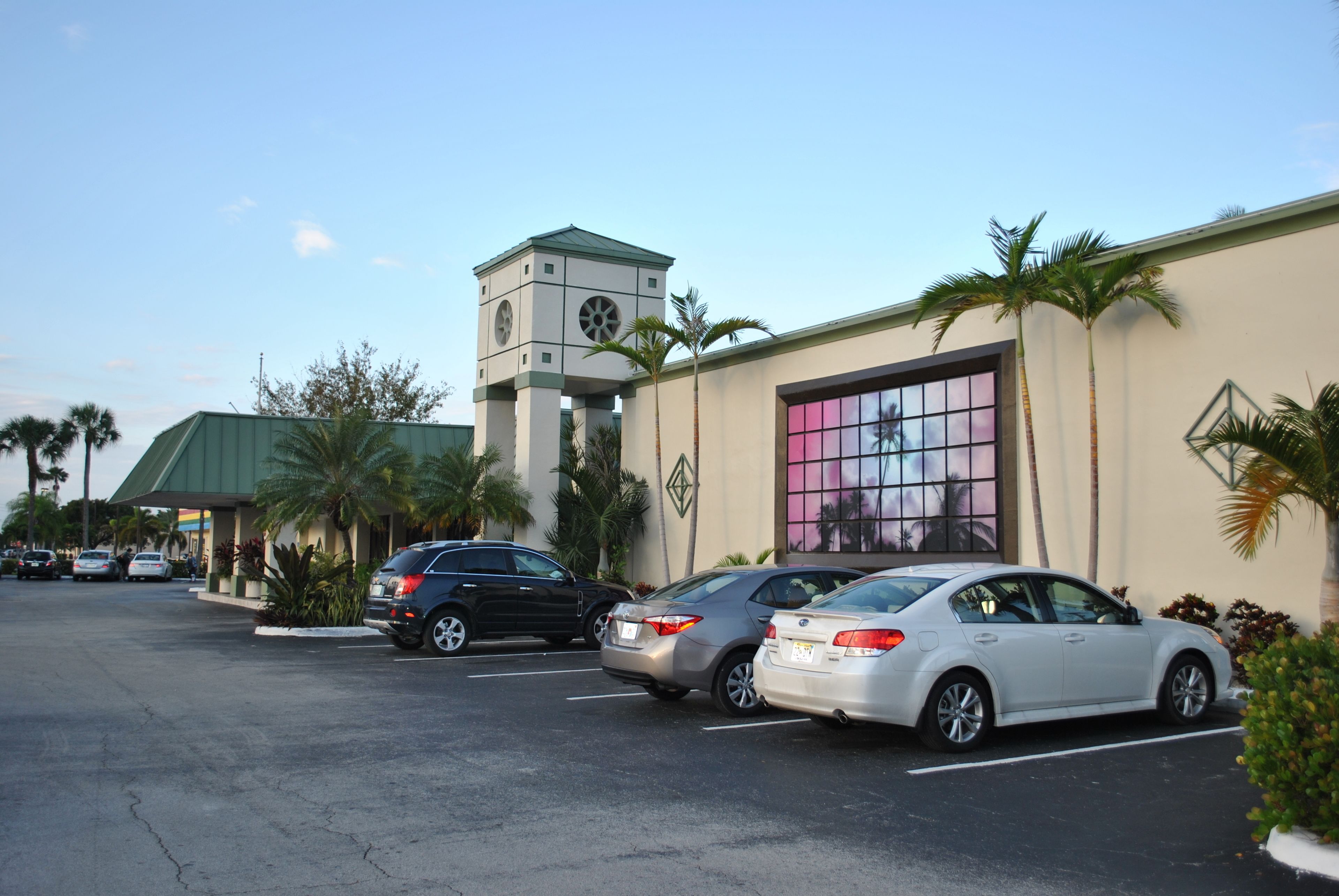 A parking lot with several cars, a building with a clock tower, and palm trees.