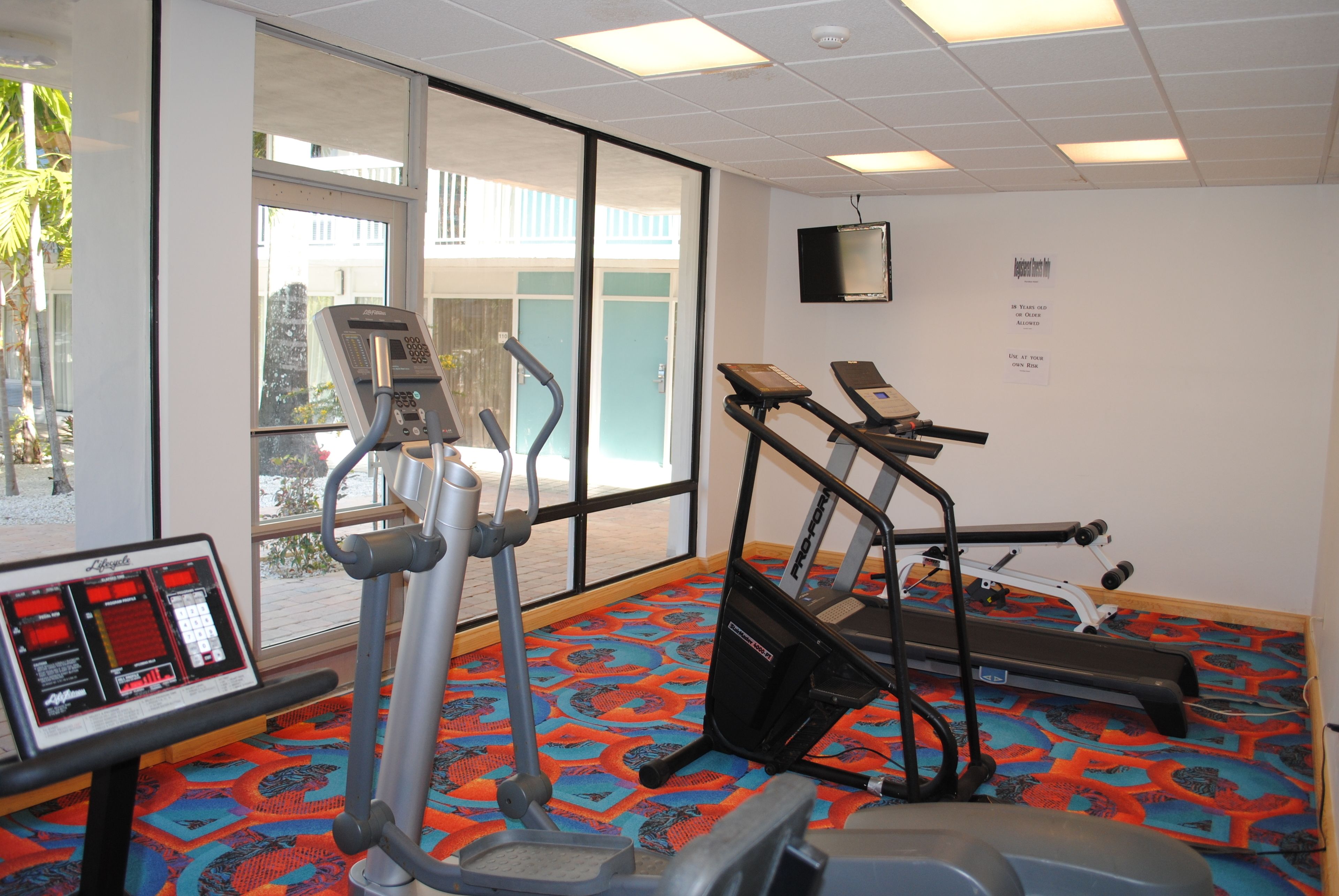 A gym with exercise equipment, a control panel, and large windows.