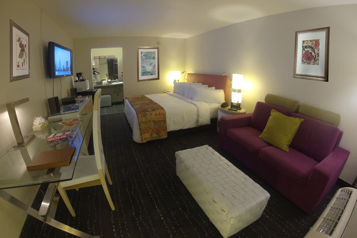 A hotel room with a bed, a desk with a computer, a couch, and a TV.