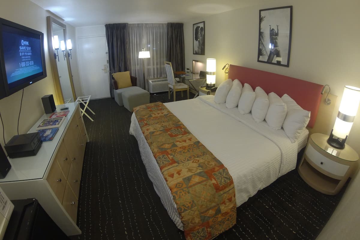 A hotel room with a bed, a desk with a computer, a chair, a TV, and a lamp.
