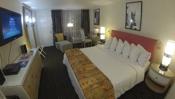 Habitación de hotel con cama, escritorio, computadora, silla, televisor y lámpara.