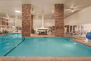 Une piscine dont la partie centrale est légèrement en contrebas, entourée de chaises longues et d’une structure composée de colonnes en briques.
