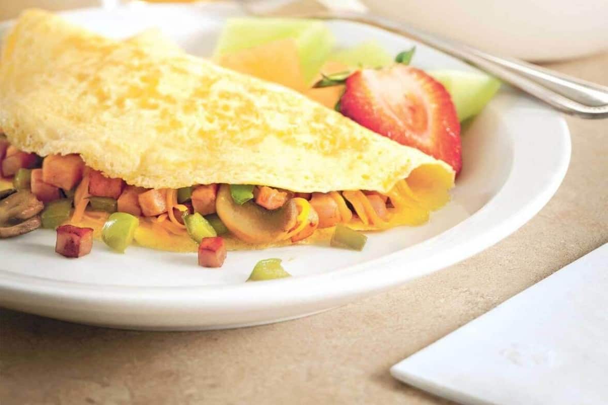 Une assiette de petit-déjeuner comprenant une omelette, des légumes et des fruits, un verre de jus d’orange et un bol de fruits rouges.