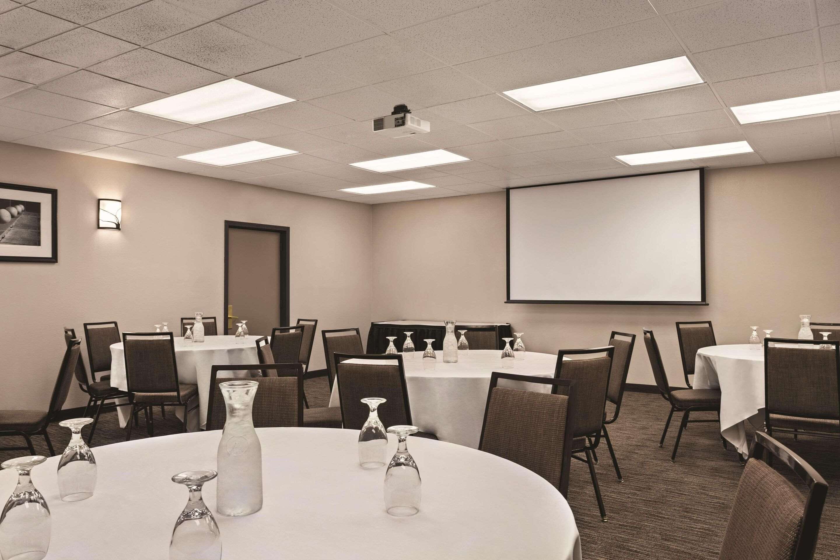 A conference room with multiple tables, chairs, and a projector screen.