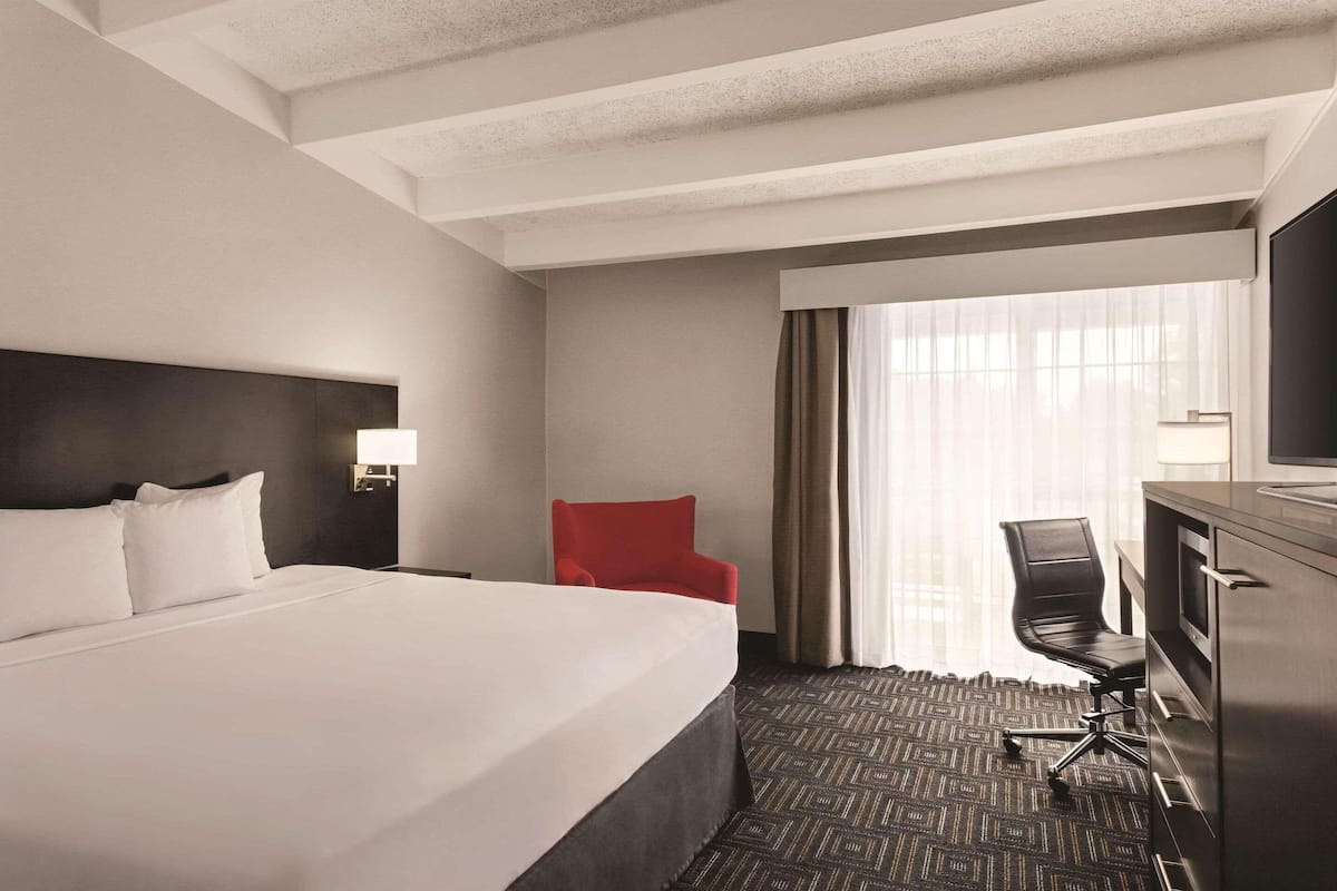 Une chambre d’hôtel avec un grand lit, un bureau avec une chaise, une télévision et une fenêtre avec des rideaux.
