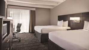 Een hotelkamer met twee bedden, een bureau met stoel, een televisie en een raam met gordijnen.