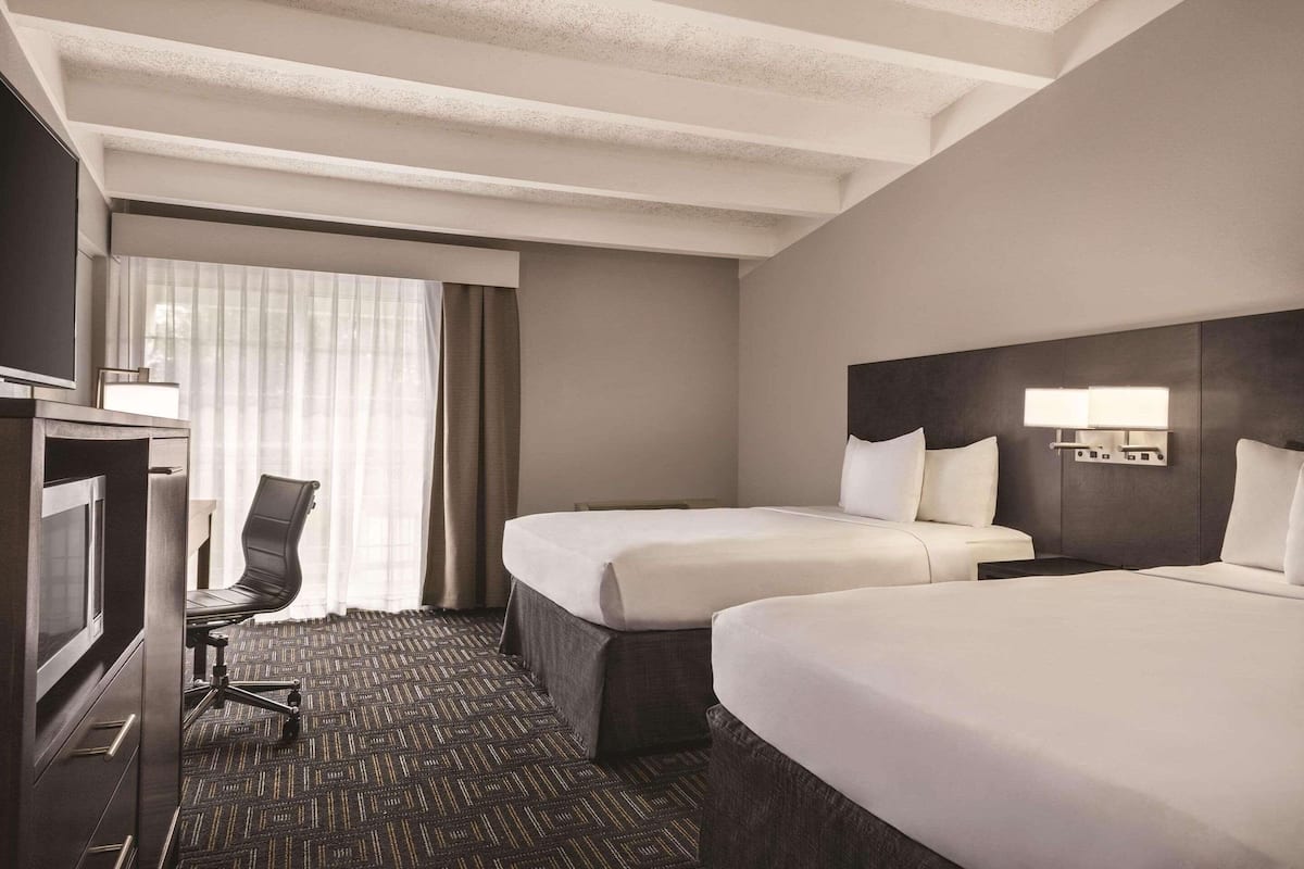 Une chambre d’hôtel avec deux lits, un bureau avec une chaise, une télévision et une fenêtre avec des rideaux.