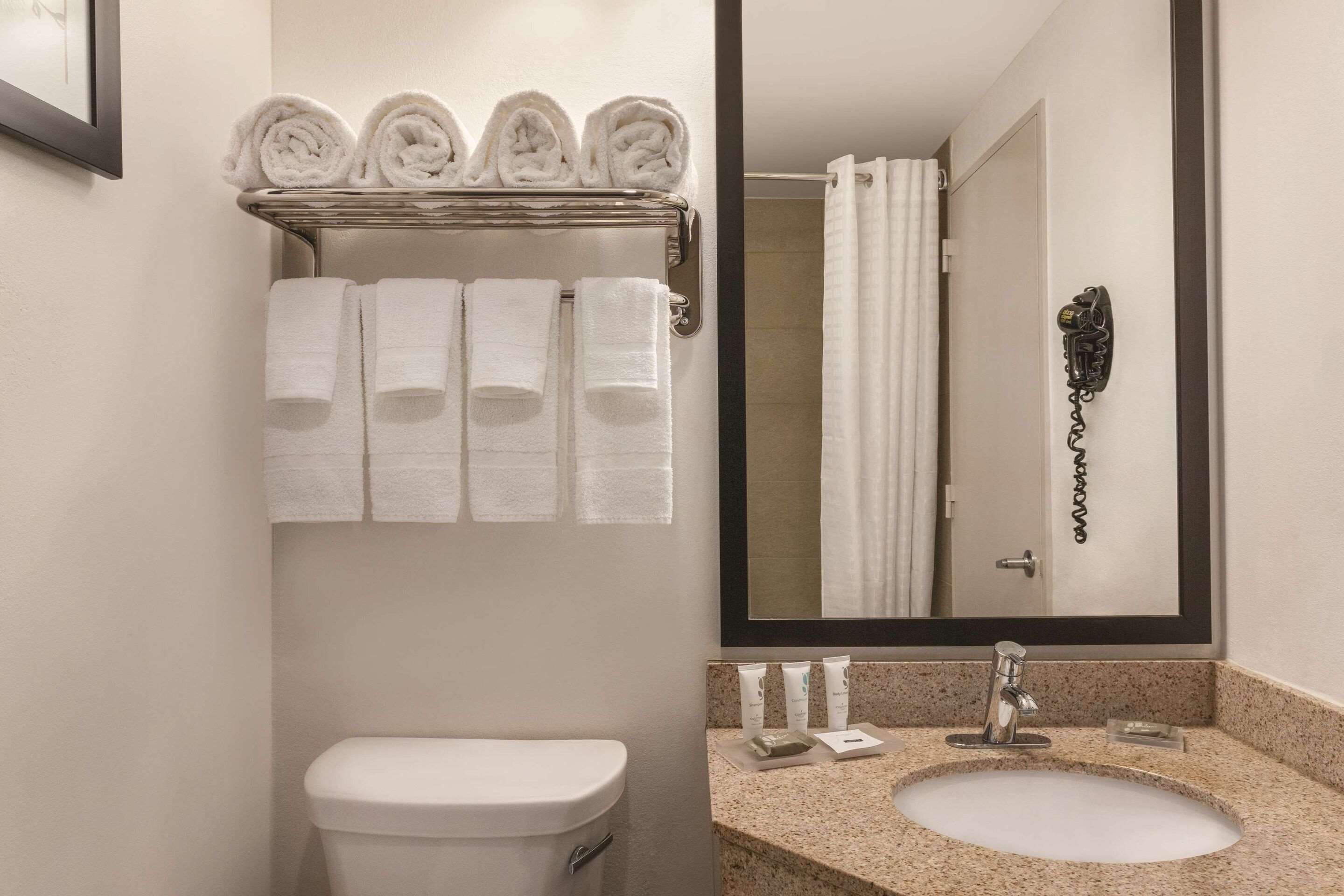 A bathroom with a toilet, a sink with a mirror, and a towel rack with neatly folded towels.