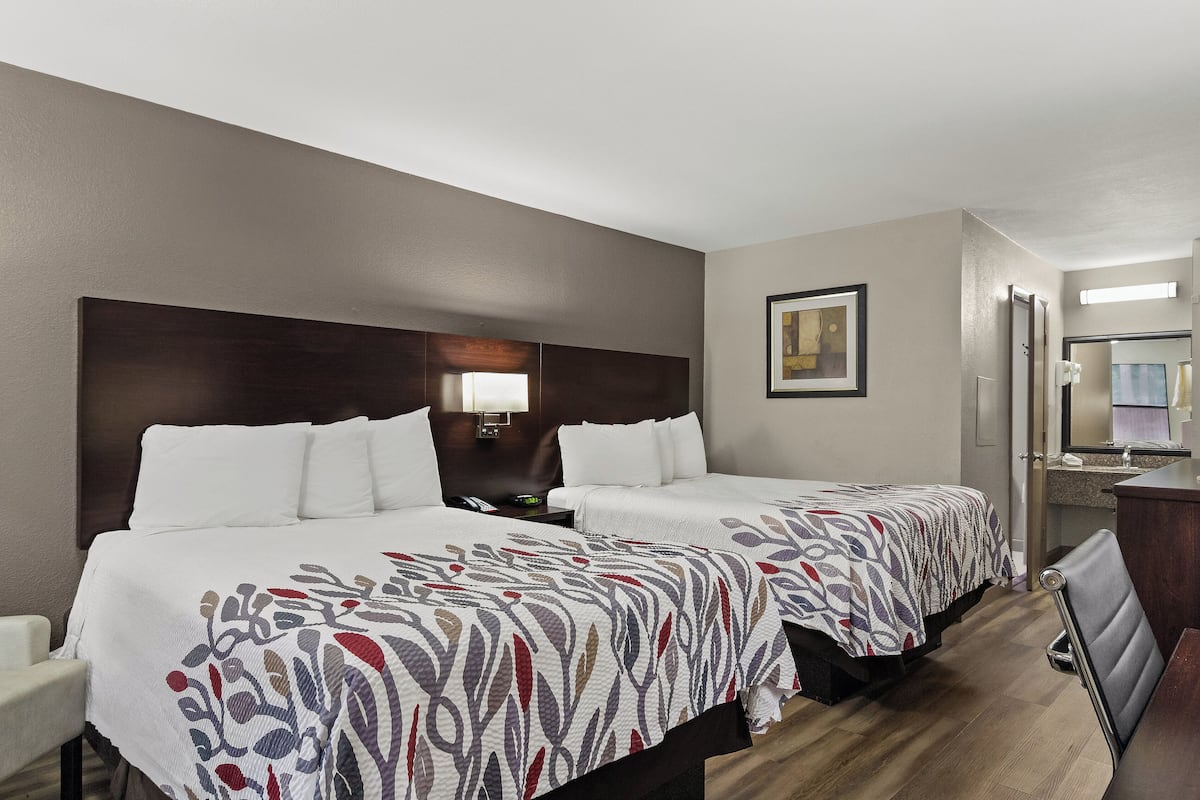 A hotel room with two beds, a desk, a chair, a mirror, and a framed picture on the wall.