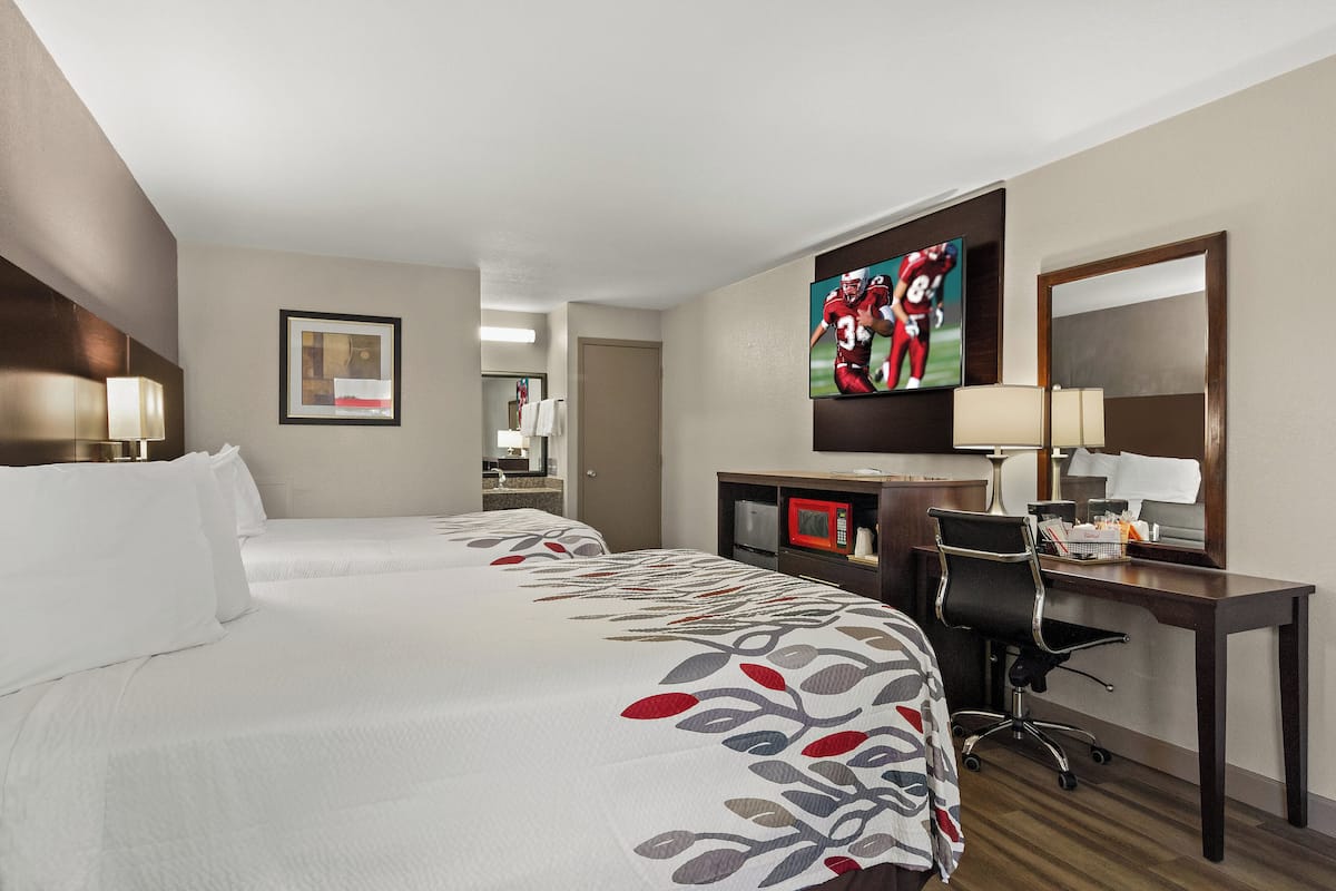 A hotel room with two beds, a desk, a chair, a TV, and a mirror.