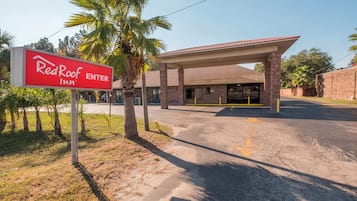 Placa da Red Roof Inn, área de estacionamento coberta e um edifício com fachada de tijolos.