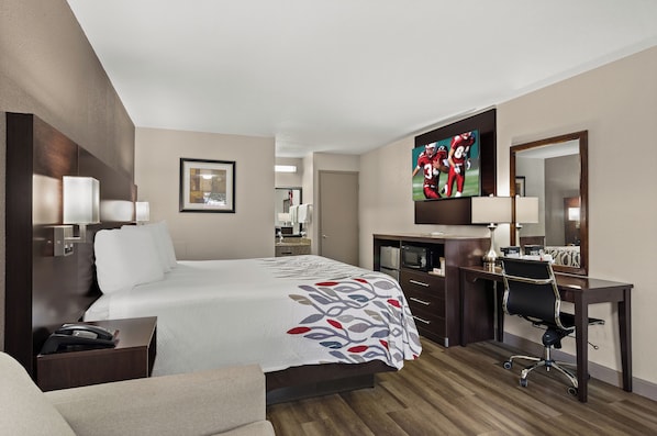 Una habitación de hotel con una cama grande, un escritorio con una silla, un televisor y un espejo.