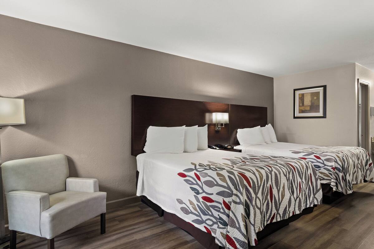 Habitación de hotel con dos camas, una silla, una lámpara y un cuadro en la pared.