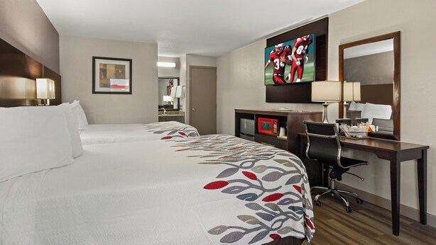 A hotel room with a large bed, a desk with a computer, a TV, and a mirror. - Red Roof Inn Baldwin (Jacksonville)
