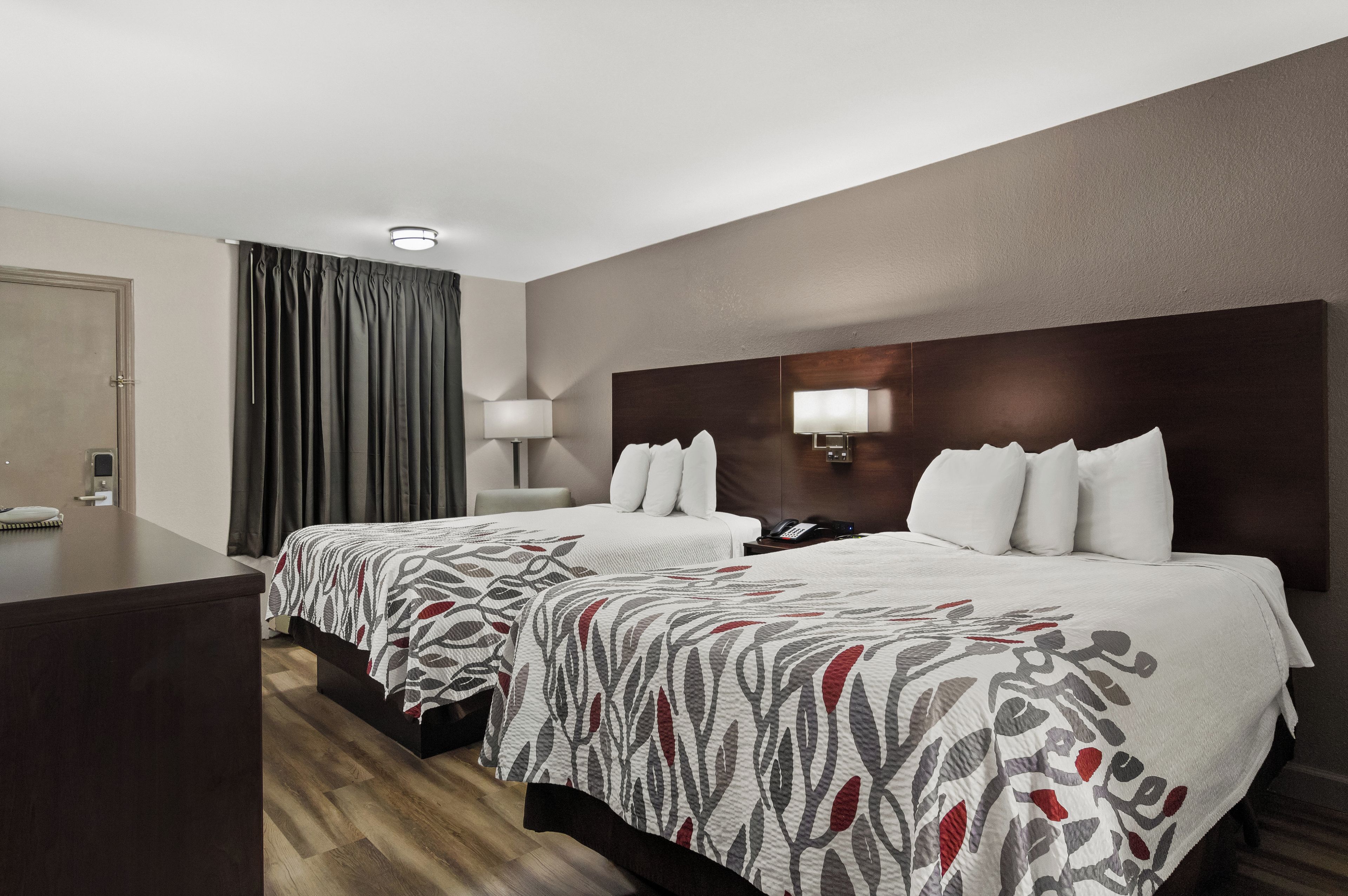 A hotel room with two beds, a desk, a lamp, and a telephone.