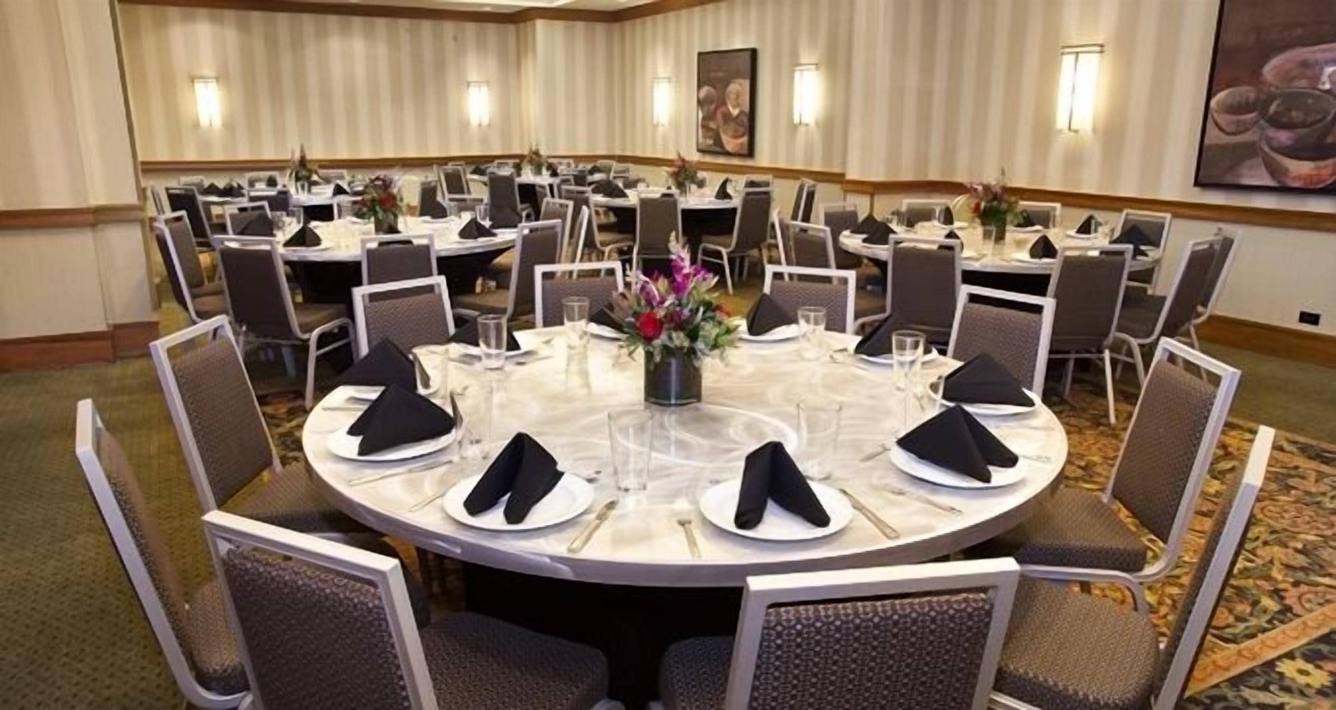 A conference room with round tables, each set with white plates, black napkins, and glassware.