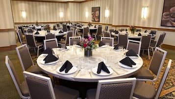 A conference room with round tables, each set with white plates, black napkins, and glassware.