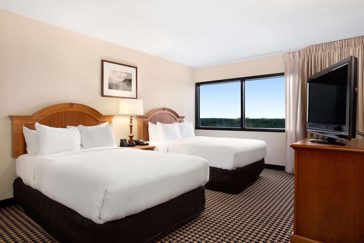 A hotel room with two beds, a TV, a window with a view, and a framed picture on the wall.
